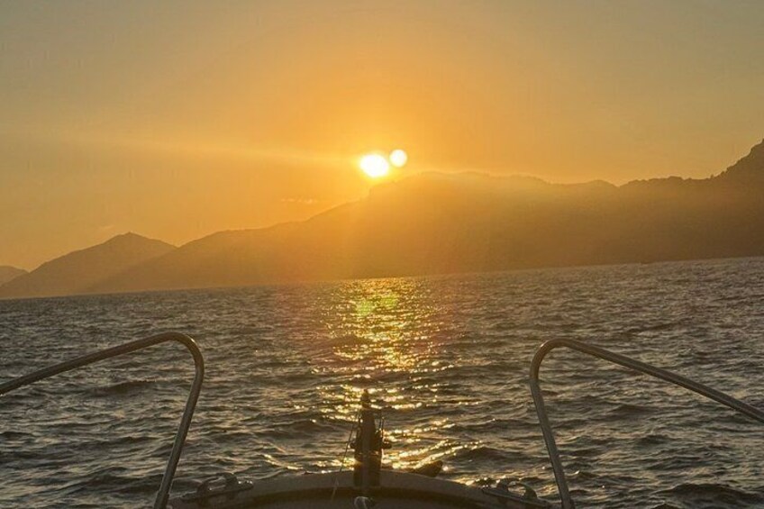 A boat with metal railings, a calm sea, and a sunset with the sun low on the horizon. 4