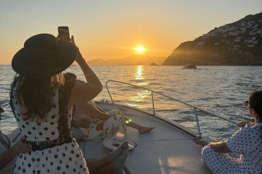 A sunset over a body of water with boats, a person taking a photo, and a person sitting on the deck. 5