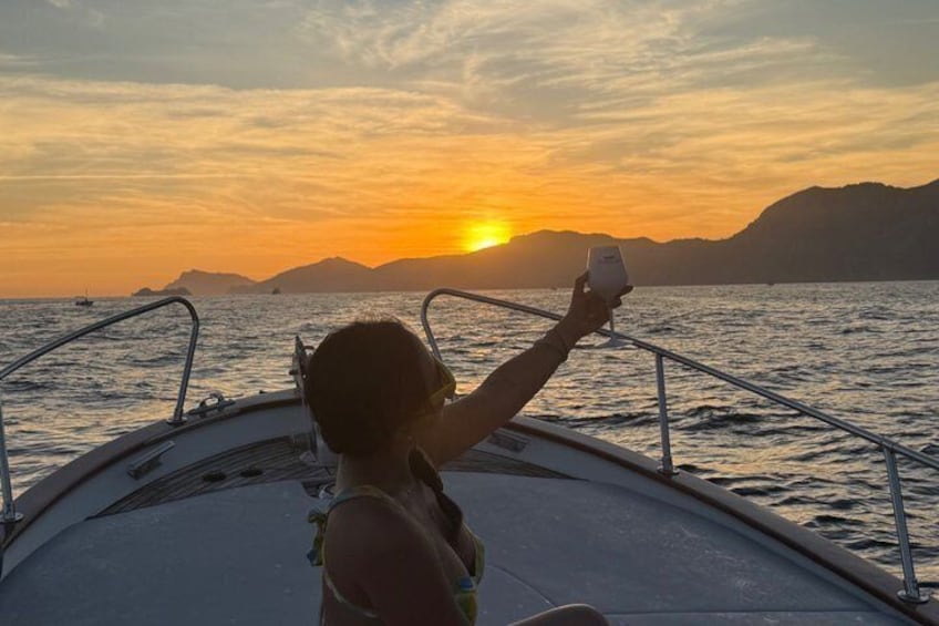 A person on a boat taking a photo of a sunset over water with mountains in the background. 2