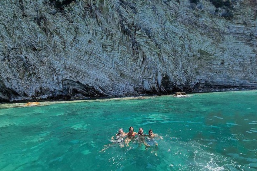A group of people swimming in clear turquoise water with a rocky cliff in the background. 2