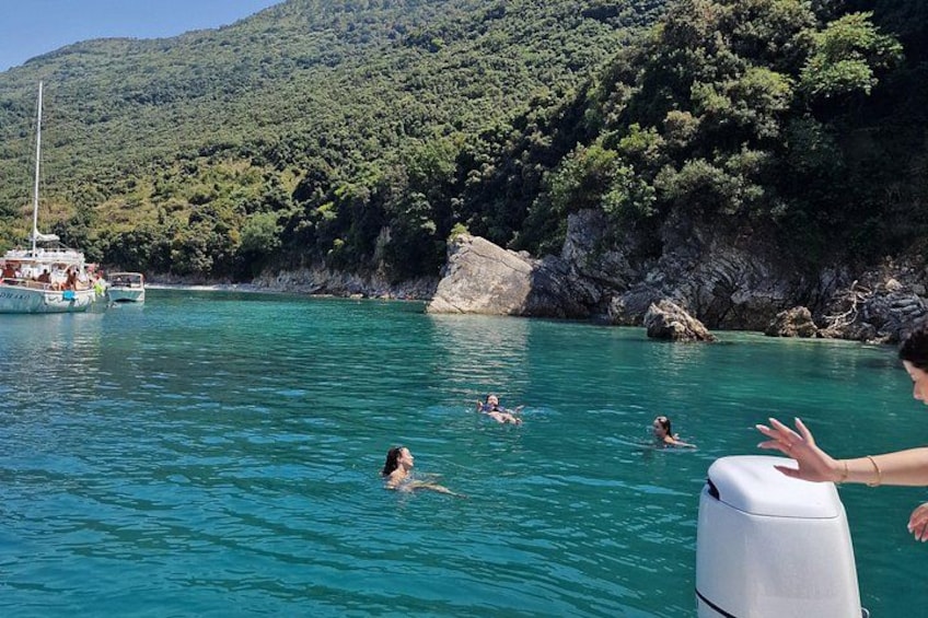 A clear turquoise sea with people swimming and a boat docked near a rocky coastline. 4