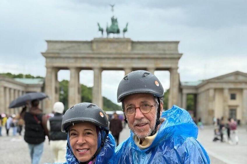 Twee personen met regenjassen en helmen voor de Brandenburger Tor. 1