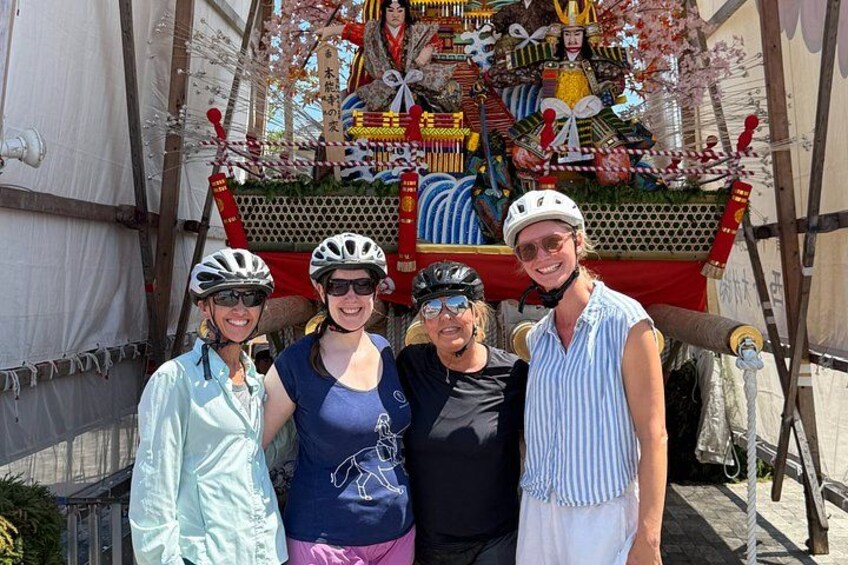 A group of people in front of a traditional Japanese festival float with intricate decorations and a large, ornate structure. 2