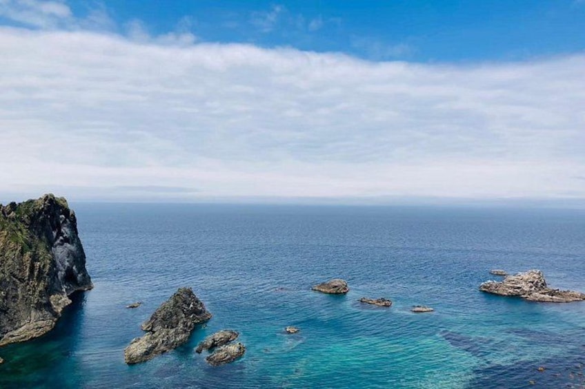 A coastal landscape with clear blue waters, rocky outcrops, and a distant horizon. 4