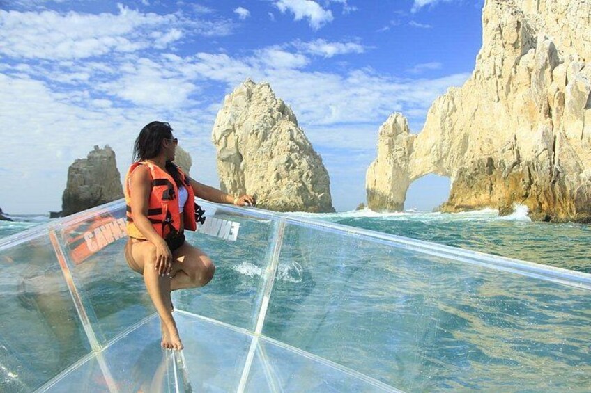 A person on a glass-bottomed boat with a life jacket, rocky cliffs, and clear blue water. 2
