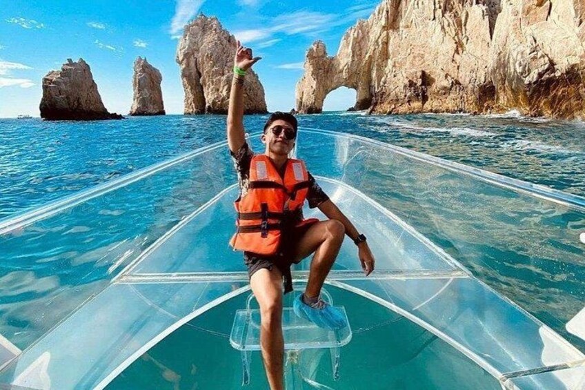 A person on a transparent boat in clear blue water with rocky formations in the background. 4