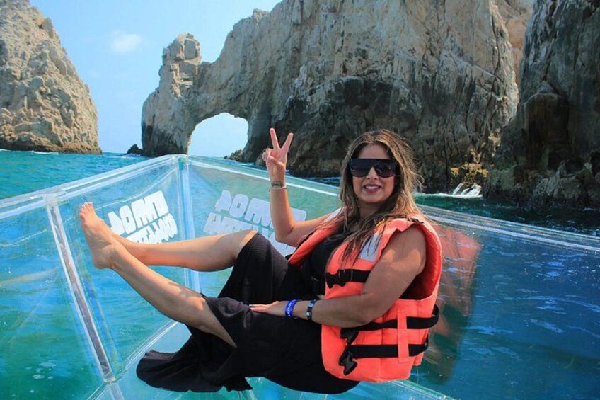A person sitting on a transparent boat with a life jacket, surrounded by clear blue water and rocky cliffs. 3