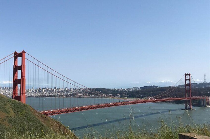 A red suspension bridge spanning a body of water with a cityscape in the background. 5
