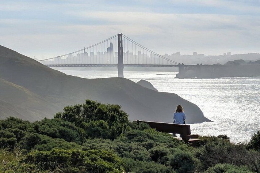 A person sitting on a bench overlooking a bridge and water. 4