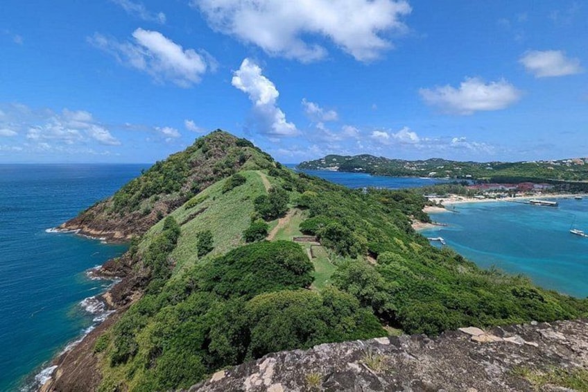 Paesaggio costiero con una collina evidente, mare blu intenso e una piccola isola con barche. 1