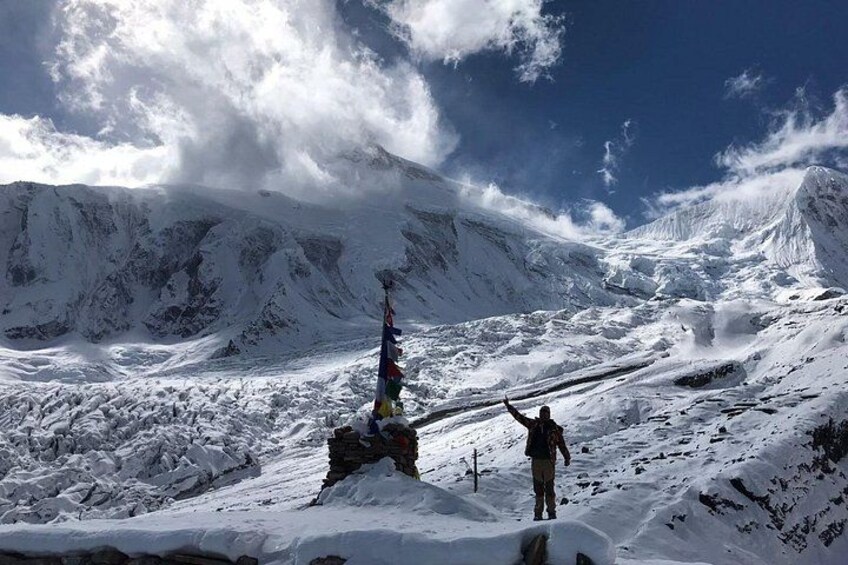 A snow-covered mountain landscape with a person standing on a snow-covered slope, a flagpole with a flag, and a clear blue sky. 4