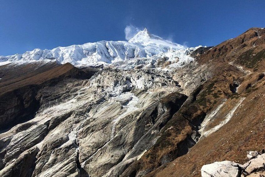A snow-covered mountain peak with rocky terrain and a clear blue sky. 3