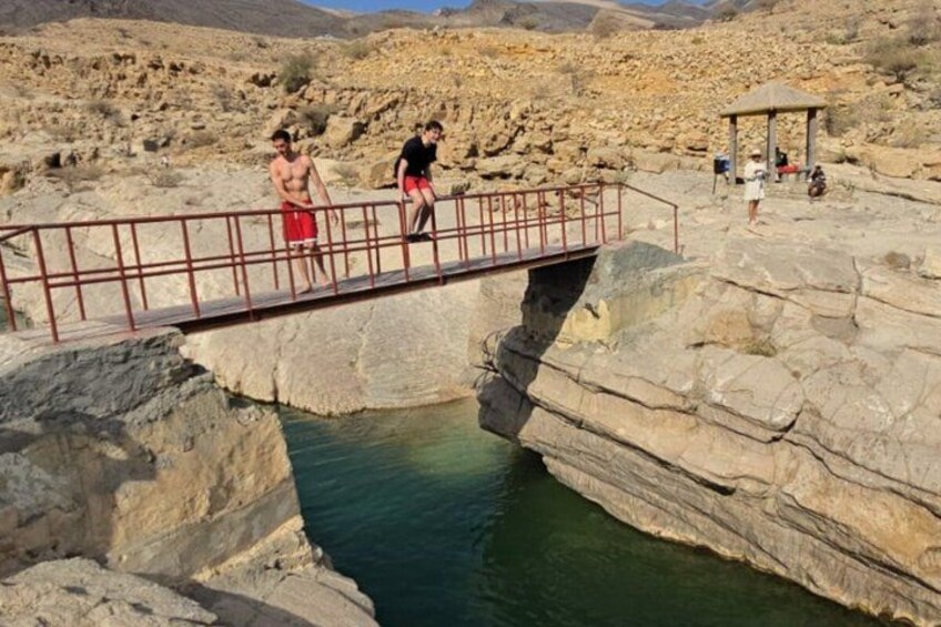 A rocky landscape with a bridge over a water body, a gazebo, and people walking. 4