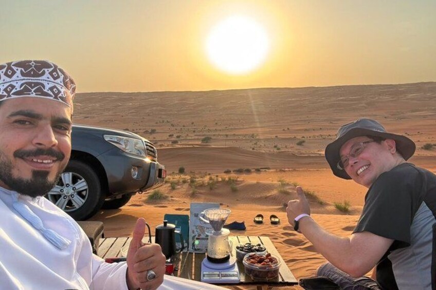 Two people sitting at a table with a desert landscape and a car in the background. 5