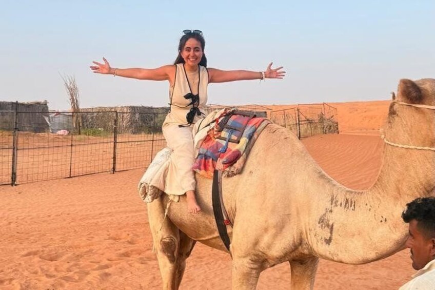 A person riding a camel in a desert setting with a fence in the background. 2