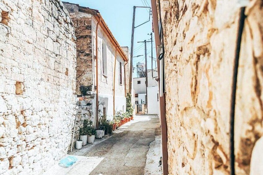 A narrow street with stone walls, potted plants, and buildings with white and red roofs. 3