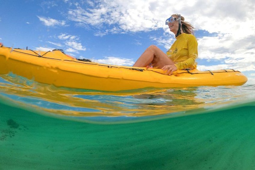 A person in a yellow kayak on clear turquoise water with a blue sky and clouds above. 2