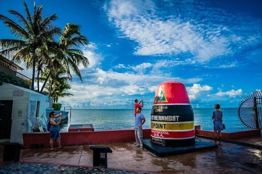 Une grande bouée rouge et jaune sur laquelle est inscrit « Point le plus au sud », une plage bordée de palmiers et des personnes près de l’eau. 5