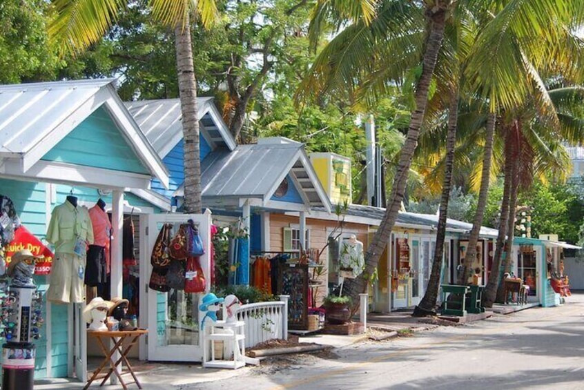 Une rangée de boutiques colorées au bord de la plage, avec des palmiers et un ciel dégagé. 2