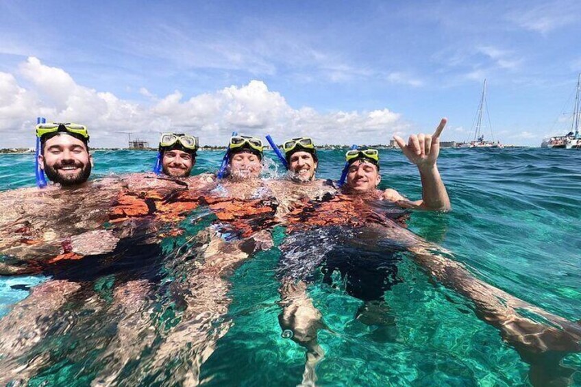 Four people snorkeling in clear blue water with a rocky underwater landscape. 4
