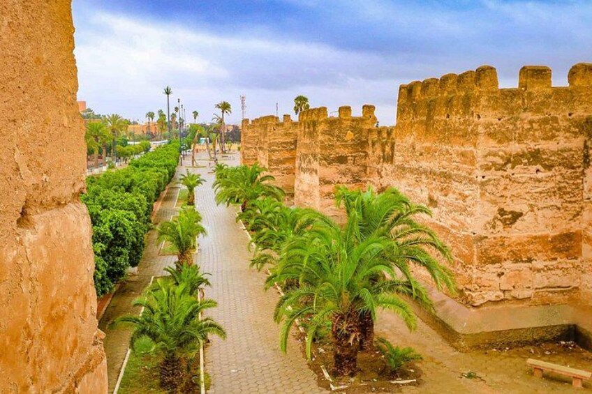 A pathway lined with palm trees and a historic stone wall. 2