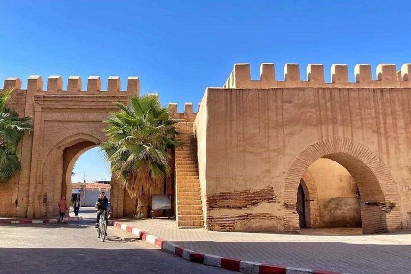 A historic stone gate with arches, palm trees, and a cyclist. 5