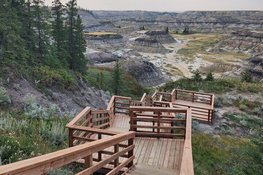 A wooden observation deck overlooking a vast, rugged landscape with layered rock formations and sparse vegetation. 1