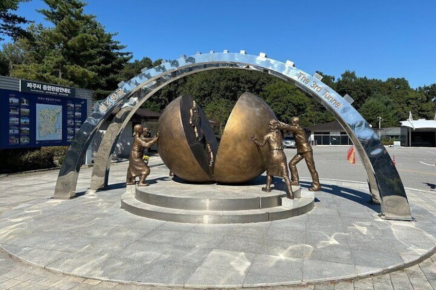 A bronze sculpture with two figures climbing a large sphere, surrounded by an archway with inscriptions. 2