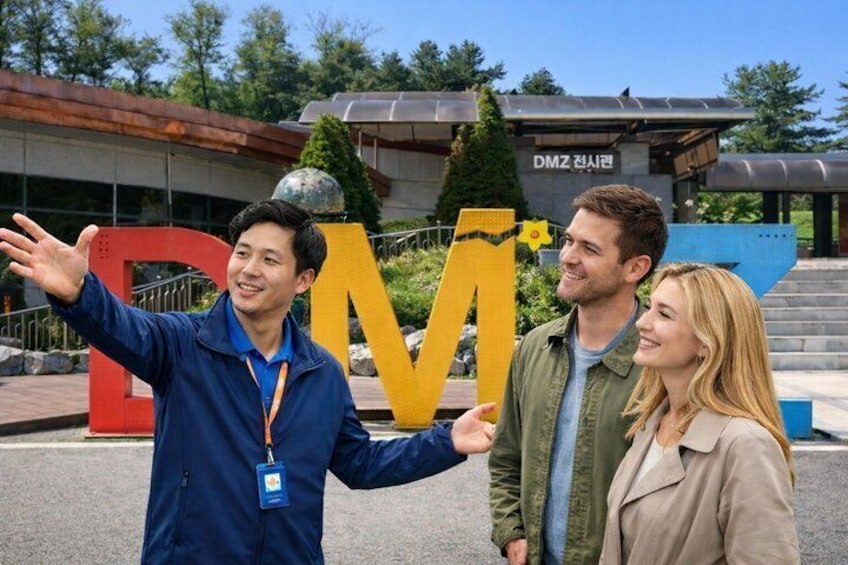 Three people standing in front of a large 'M' sign with a building in the background. 1
