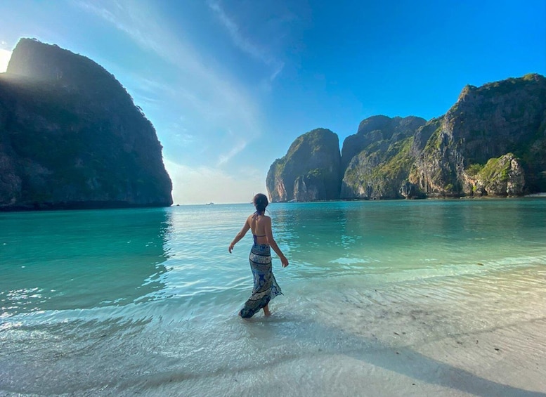 A person walking on a beach with clear turquoise water and rocky cliffs in the background. 2