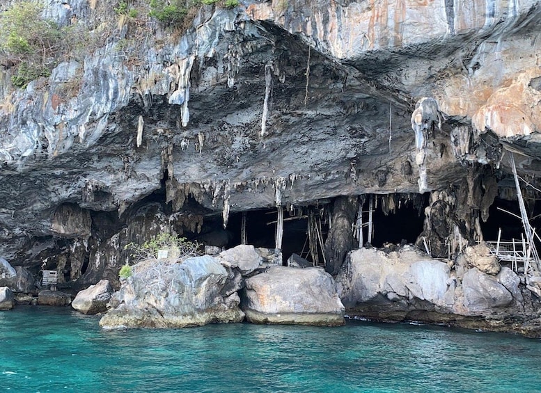 A cave entrance with stalactites and stalagmites, surrounded by large rocks and clear turquoise water. 5
