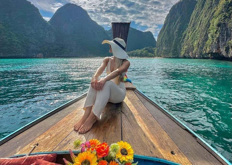 A person sitting on a wooden boat with a hat, surrounded by a mountainous landscape and turquoise water. 1