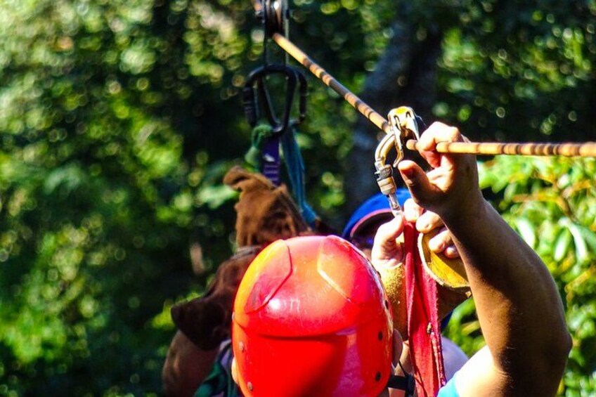 A person wearing a red helmet and harness, preparing for a zip-lining activity in a forested area. 1