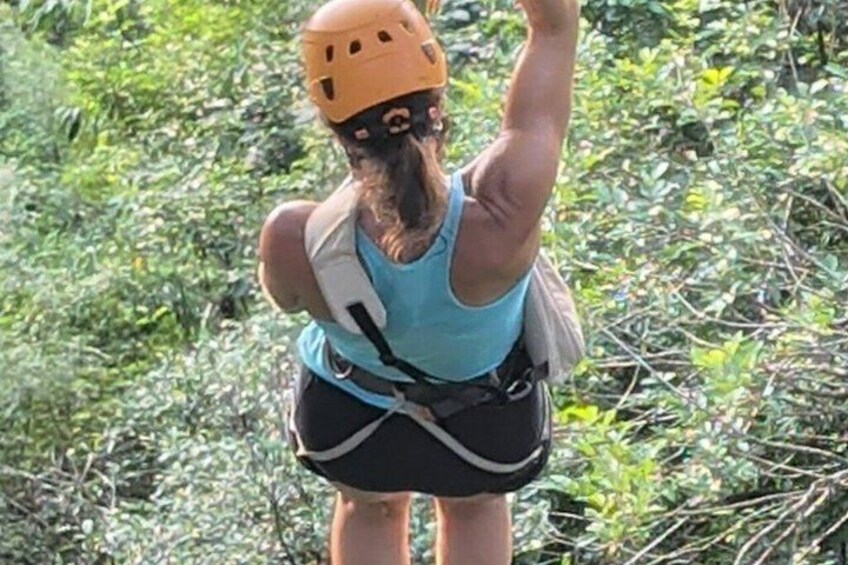 A person wearing a helmet and harness, standing in a natural environment with dense foliage. 4