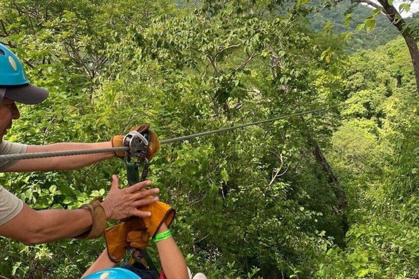 A person in a forested area, wearing a helmet and harness, being assisted by another person. 2