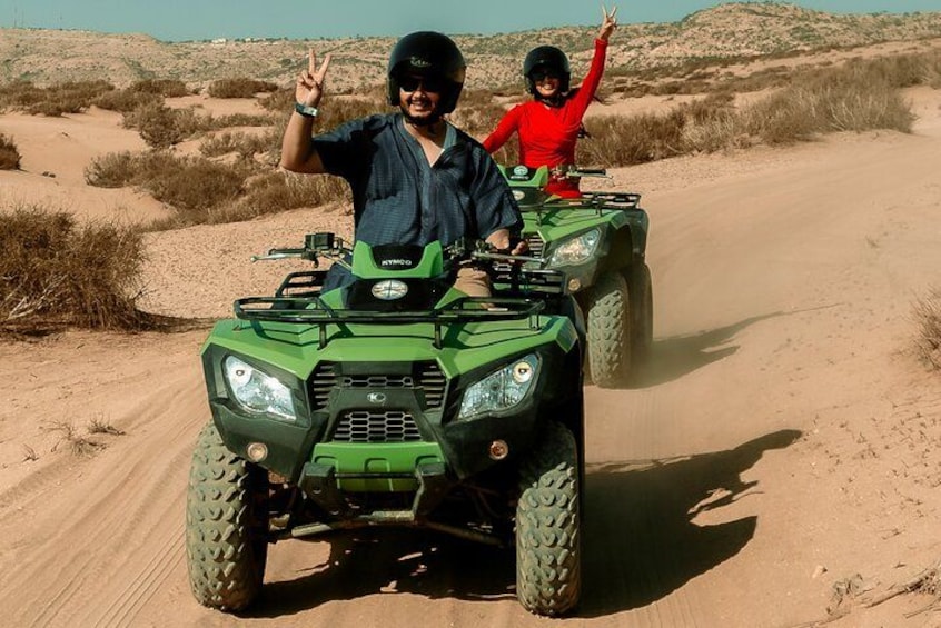 Two people on an ATV in a desert with sand dunes. 1