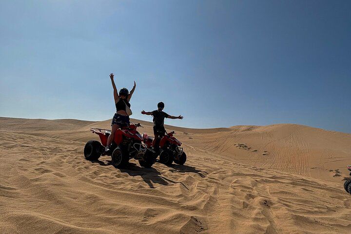 Two people on red ATVs in a desert with sand dunes. 3
