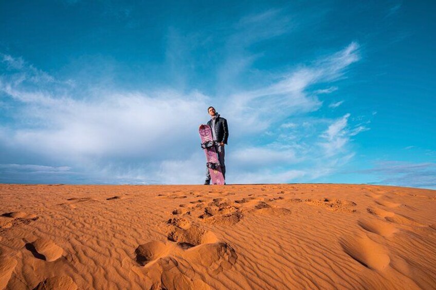 A person standing on a sandy desert with footprints, under a clear blue sky. 2