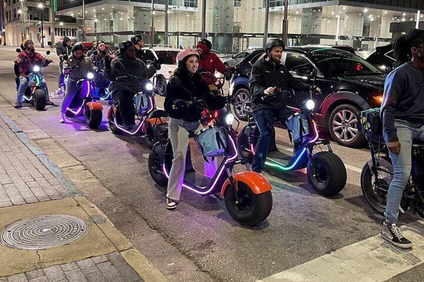 People riding electric scooters with neon lights on a city street at night. 2