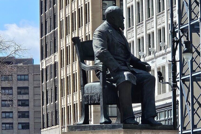 Une statue représentant un homme assis, vêtu d’un costume, sur un banc. 2