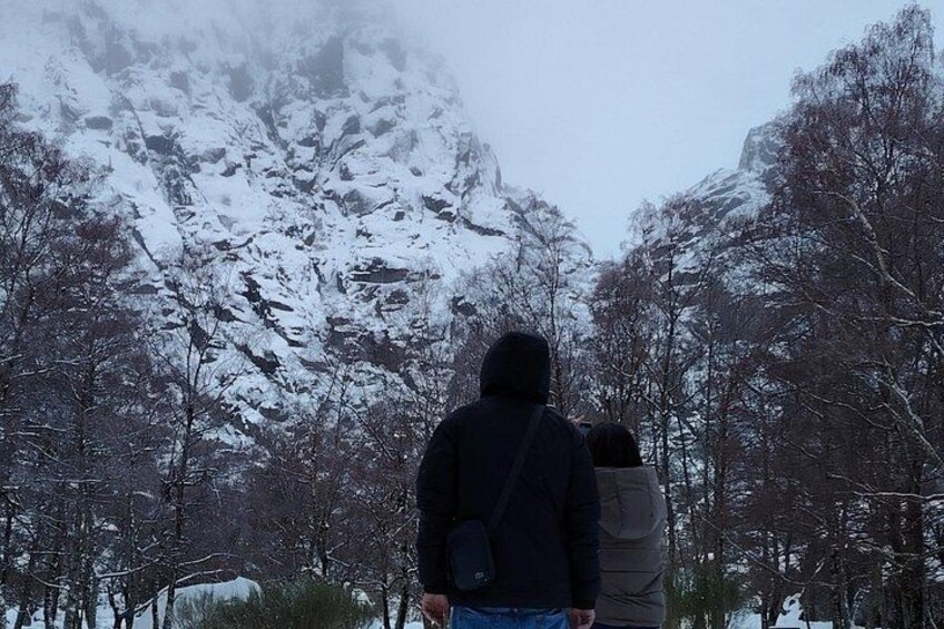 A person walking with a child in a snowy forest with snow-covered trees and mountains in the background. 4