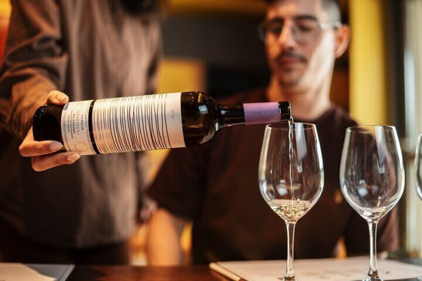 A person pouring wine from a bottle into two wine glasses. 3