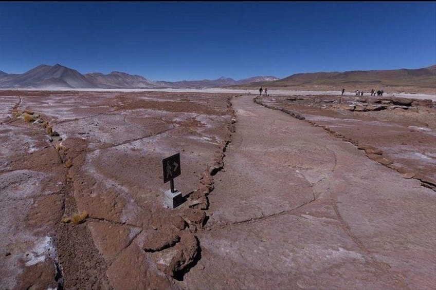 A dry, cracked landscape with a signpost and distant mountains. 4