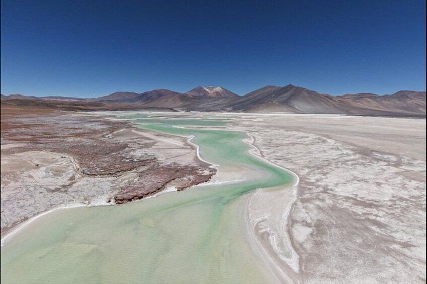 A river winding through a salt flat with mountains in the background. 2
