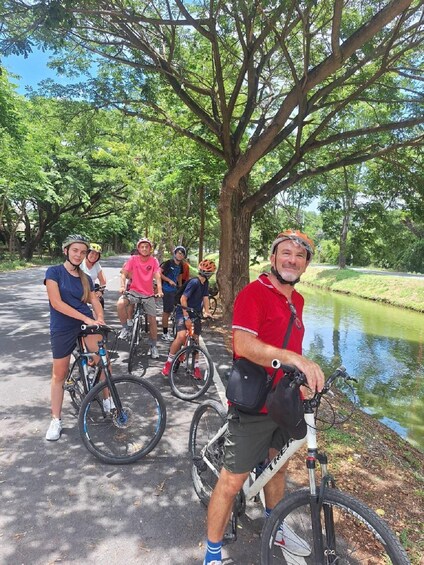 A group of cyclists on a paved path with trees and a body of water in the background. 5