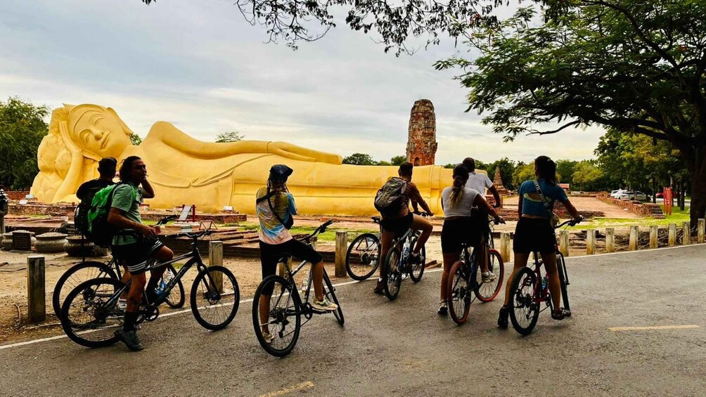 A group of cyclists on a paved path with a large golden statue in the background. 5