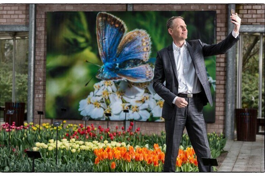 A man taking a selfie in front of a large butterfly painting and colorful flowers. 1