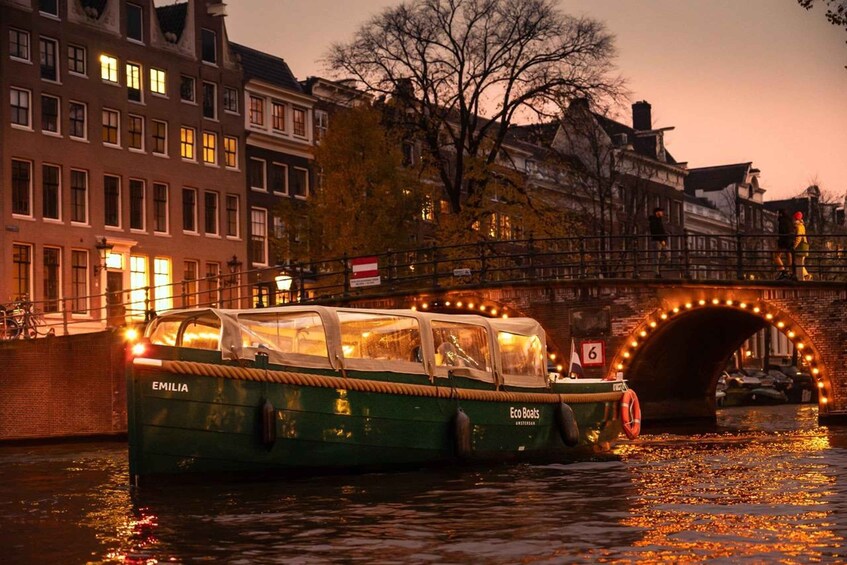 A green boat named EMILIA on a canal, with a bridge and buildings in the background. 5