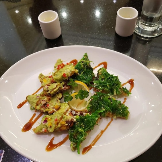 A white plate with a dish of avocado slices, greens, and a lemon wedge, drizzled with sauce. 5