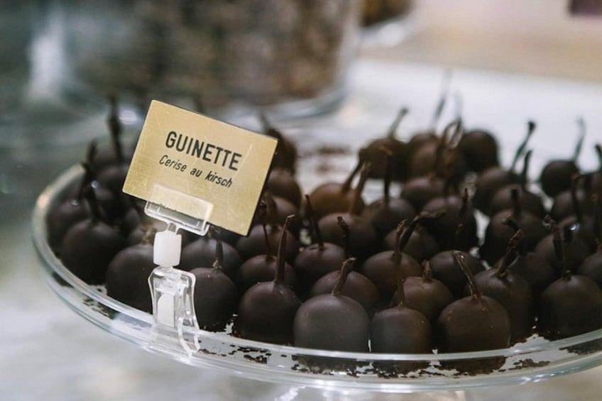 A display of dark chocolate-covered cherries with a sign labeled 'GUINETTE Cerise au kirsch.' 3